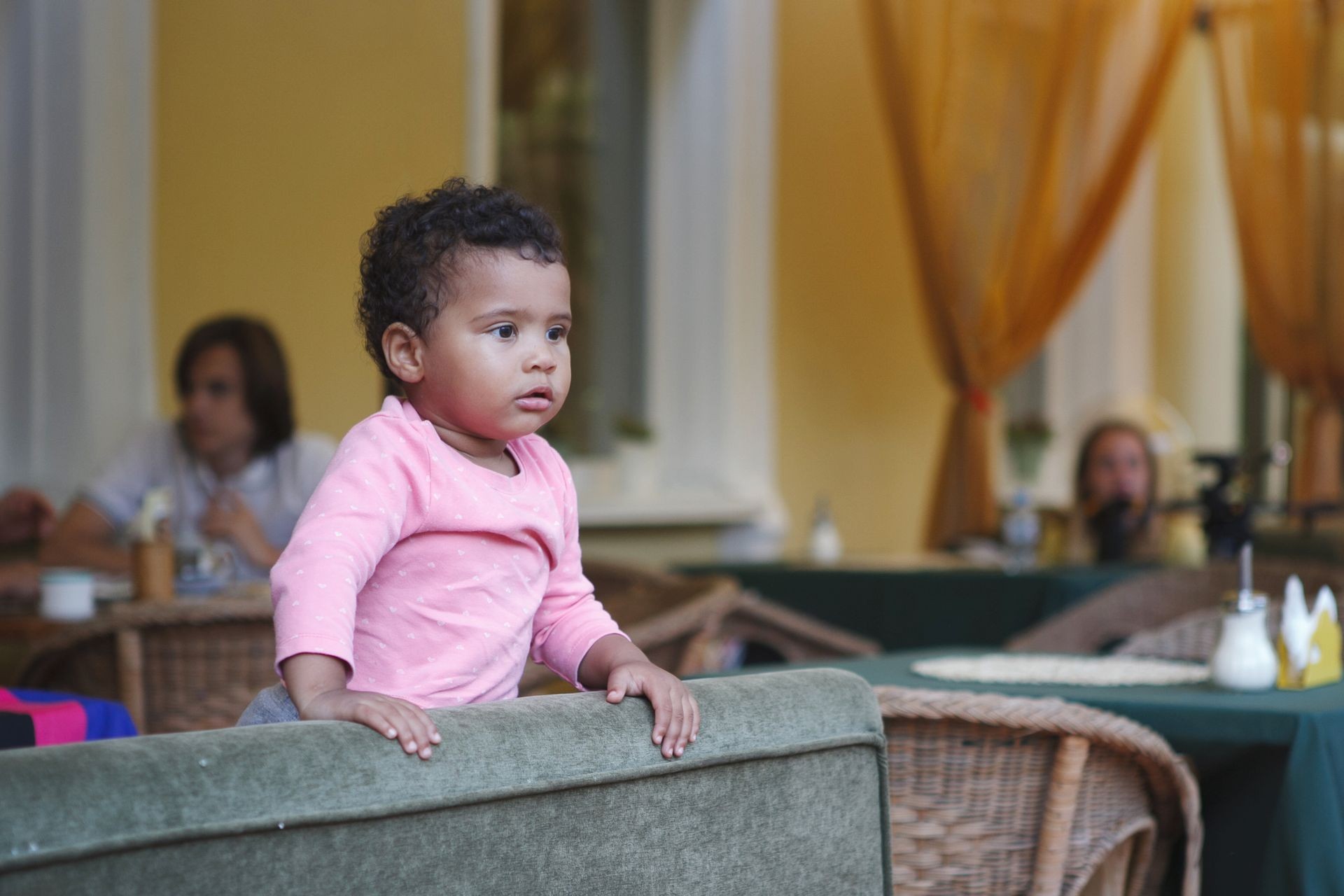 Cute black baby girl is sitting in a chair in a summer cafe.